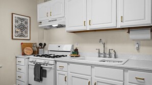 Une cuisine avec des meubles blancs, une cuisinière, un évier et un plan de travail.