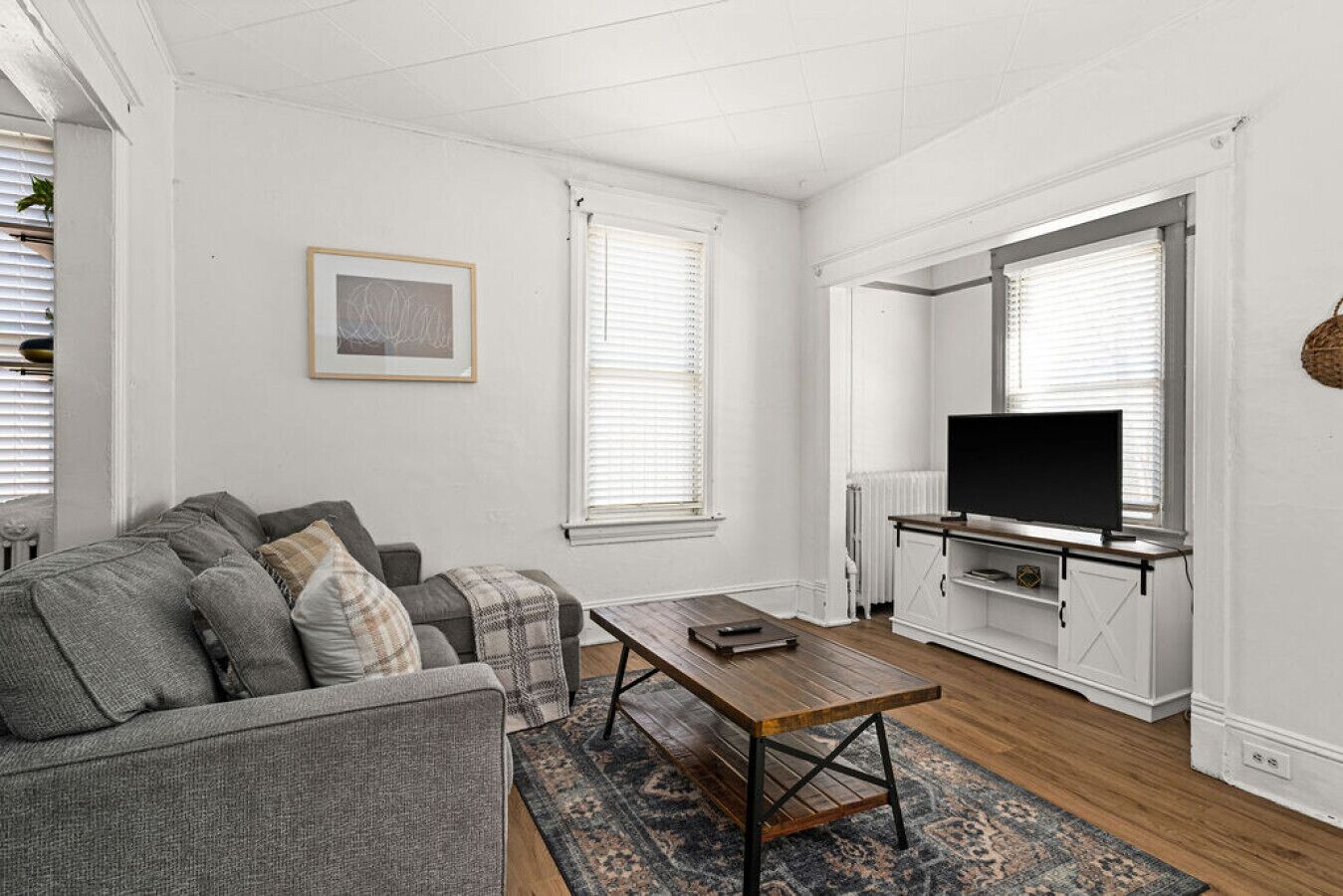 Ein Wohnzimmer mit grauem Sofa, einem Holztisch und einem Fernseher auf einem weißen Schrank.