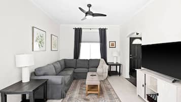 A modern living room with a sectional sofa, a flat-screen TV, a ceiling fan, and a patterned rug.
