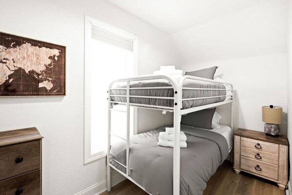 A bunk bed room with a wooden dresser, a lamp, and a world map on the wall.