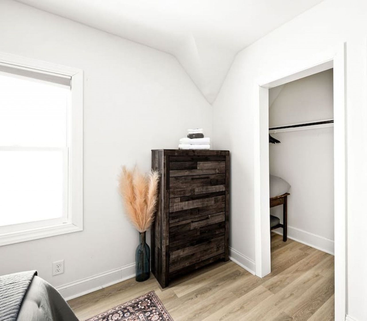 Habitació amb un armari de fusta, una finestra, una porta que dona a una altra habitació i una catifa amb dibuixos.