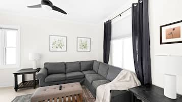 Een moderne woonkamer met een modulaire bank, een houten bankje, een plafondventilator en twee ingelijste kunstwerken aan de muur.