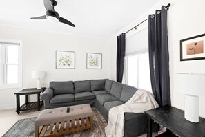 A modern living room with a sectional sofa, a wooden bench, a ceiling fan, and two framed artworks on the wall.