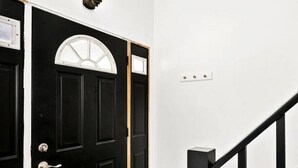 Una puerta negra con un ventanal de marco blanco, una escalera negra y una pared blanca con un interruptor de luz.