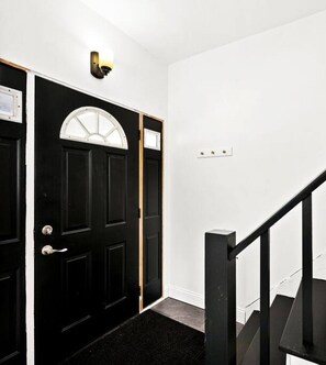 A black door with a white-framed window, a black staircase, and a wall-mounted light fixture.