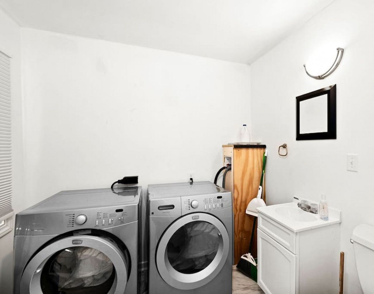 Un espace buanderie comprenant deux machines à laver à chargement frontal, un meuble en bois, un évier et des toilettes.