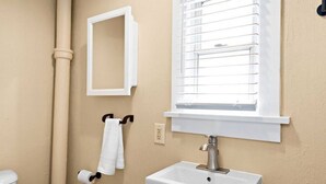 A bathroom with a white sink, a towel rack with a white towel, a toilet, and a window with blinds. - Clough · Quaint Cottage on Clough (Superior)
