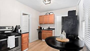 Una cocina compacta con estufa, horno, armarios de madera, un refrigerador negro y una mesa de comedor con un florero.