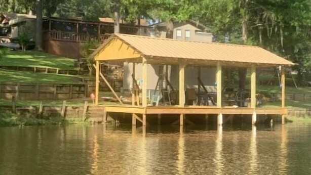 A wooden dock with a covered seating area over a body of water, surrounded by trees and a building in the background. - Lanan Hideaway on Toledo Bend >B CLOSE TO TOLEDO TOWN!!!! (Many)