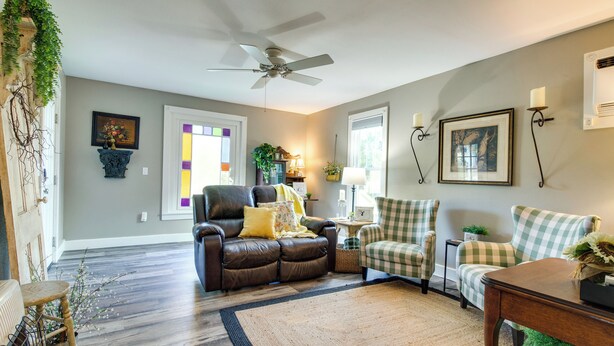 A living room with a brown leather sofa, a green and white checkered armchair, a wooden coffee table, and a ceiling fan. - Updated Cotter Cottage: Walk to White River! (Cotter)