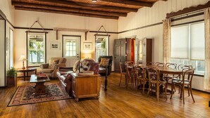 Een ruime woonkamer met houten vloeren, een eethoek met een grote houten tafel en stoelen, en een hoge plafond met zichtbare balken.