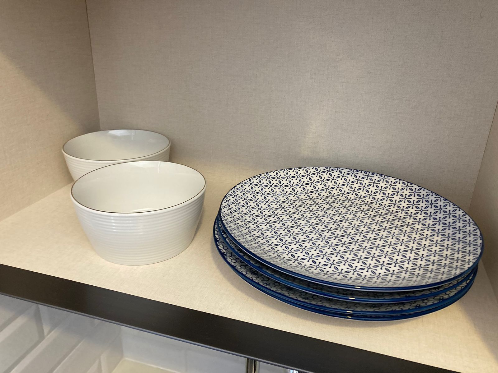 Una encimera de cocina con tres boles blancos y una pila de platos azules estampados.