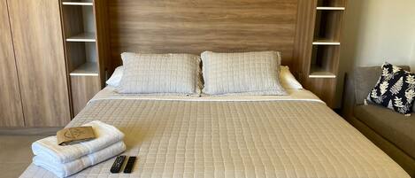 A neatly made bed with a quilted white duvet, two pillows, and a remote control on the side.