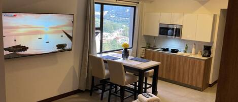 Une cuisine compacte avec un coin repas, un téléviseur fixé au mur et une vue sur l’extérieur.