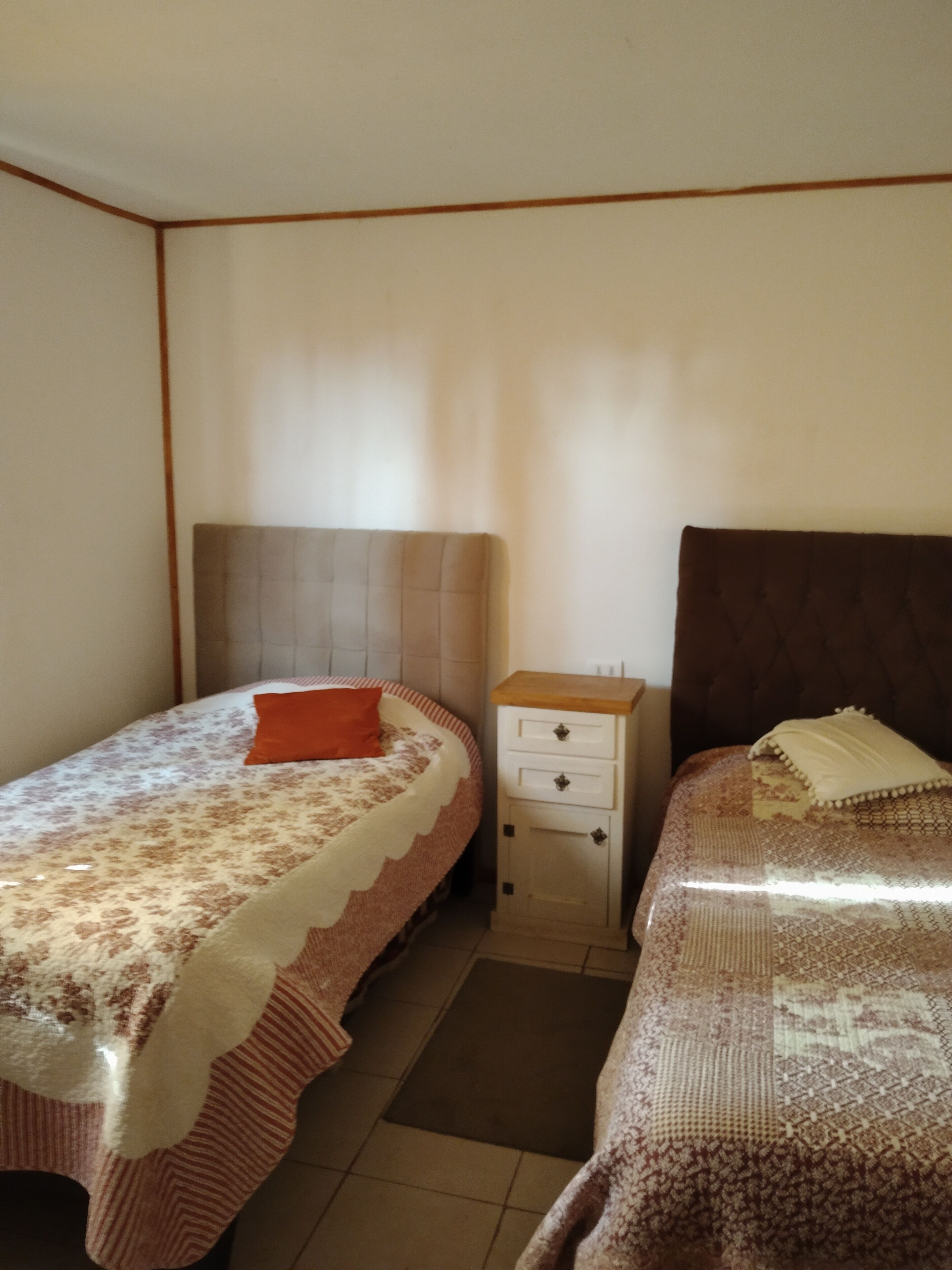Une chambre avec deux lits, une table de chevet et un petit placard.