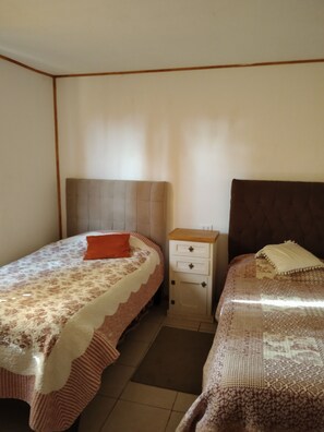 Una habitación con dos camas, una mesita de noche y un mueble pequeño.