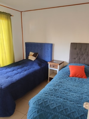 Una habitación con dos camas, una mesita de noche y un ventanal con cortinas.