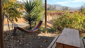 Eine Hängematte unter einer Holzpergola, eine Holzbank und ein Garten mit Blick auf ferne Hügel.