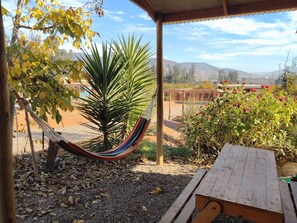 Una hamaca bajo una pérgola de madera, un banco de madera y un jardín con vistas a colinas distantes.