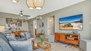 Un salón moderno con sofá, mesa de centro y un televisor grande que muestra una escena de playa.