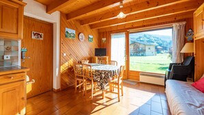 A cozy wooden cabin with a dining area, a TV, and a large window with a view of houses and greenery. - wonderful Chalet 6 ppl, mountain view (Morillon)
