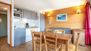A compact kitchen with modern appliances, a dining area with wooden furniture, and a cozy seating space with a wooden wall and a framed picture. - Appartement 6 pers, vue montagne avec terrasse (Chamrousse)