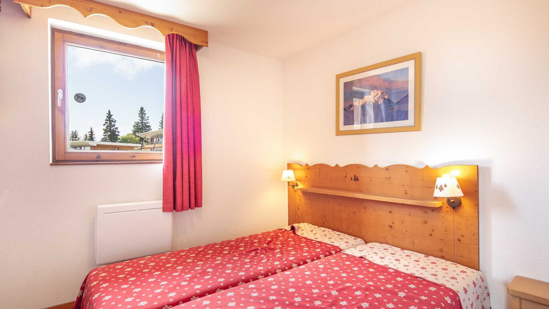 Ein Schlafzimmer mit zwei Betten, einem Fenster mit Blick auf Bäume, einem Holzkopfende und einem gerahmten Bild an der Wand.