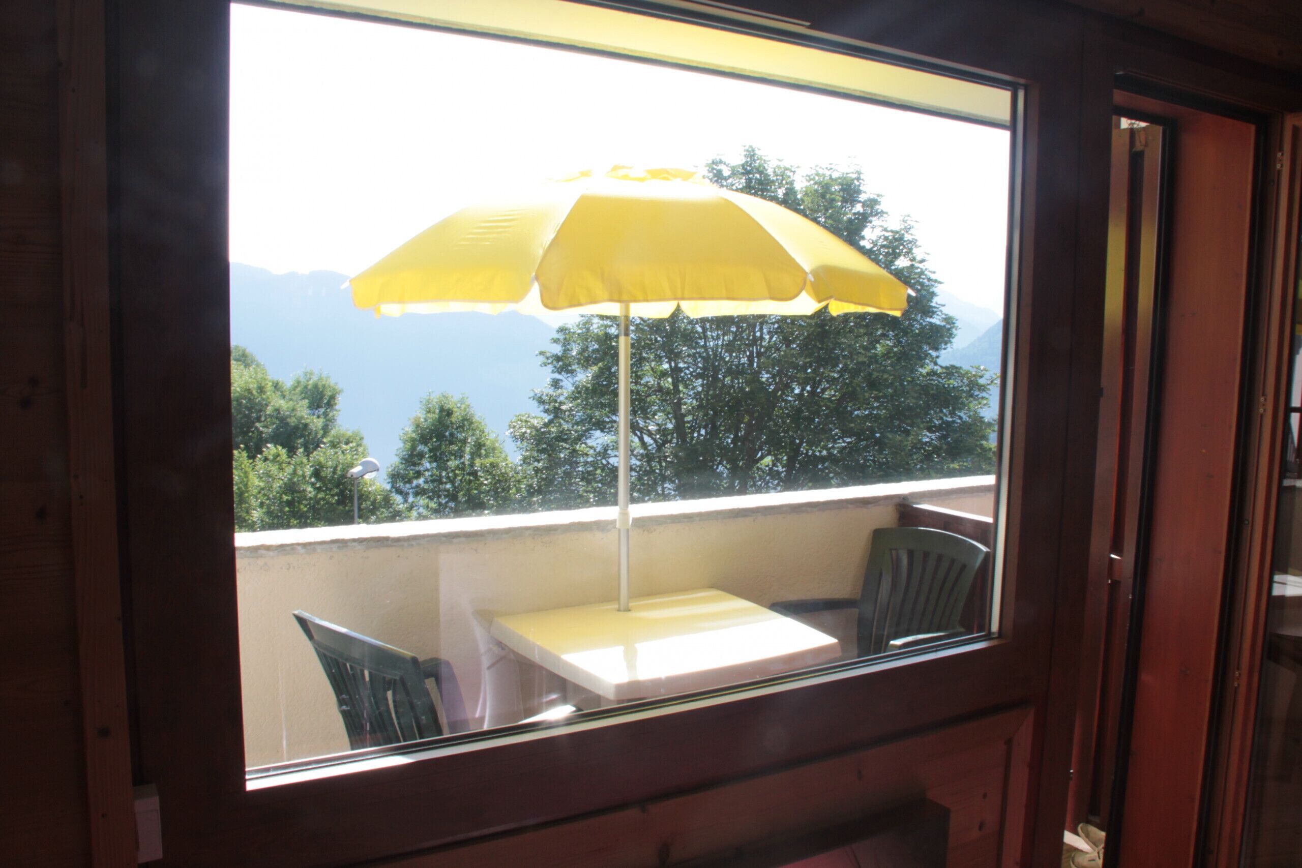 Une fenêtre, un parapluie jaune, une table et une chaise.