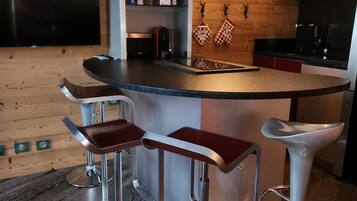Une cuisine moderne dotée d’un coin bar, de tabourets de bar en acier inoxydable, de meubles en bois et d’un four encastré.
