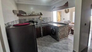 Una cocina moderna con encimera de granito, lavadora integrada y una zona de comedor al fondo.