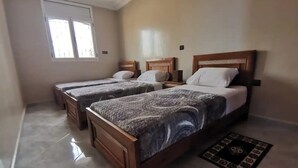 Habitación de hotel con dos camas individuales, una cama grande, un ventanal y un tapete decorativo.