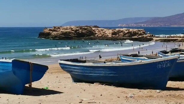 Una playa con barcos y un promontorio rocoso al fondo.
