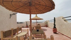 Una terraza en la azotea con muebles de mimbre, un amplio paraguas de paja y plantas en macetas.