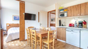 A compact hotel room with a wooden dining table, chairs, a bed, a TV, a kitchenette, and a bathroom. - Superbe logement 6 pers à Chamrousse (Chamrousse)