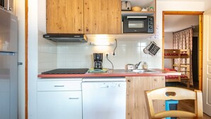 A compact kitchen with wooden cabinets, a built-in oven, a coffee maker, and a sink.