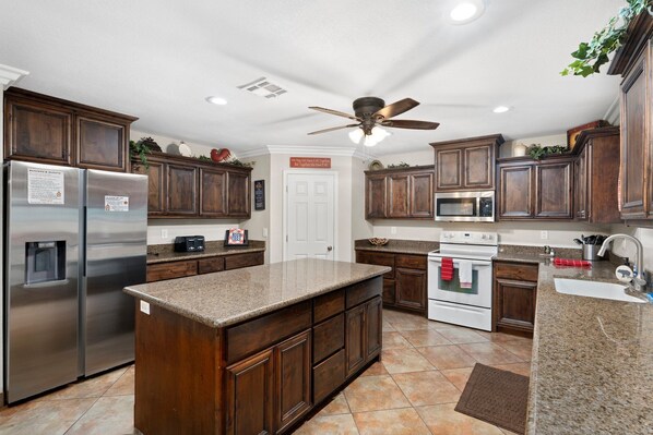 A modern kitchen with dark wooden cabinets, stainless steel appliances, granite countertops, and a central island.
