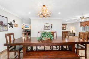 A dining area with a wooden table, chairs, a chandelier, and a television in the background. - Rainbow Lake Retreat: Lakeside Cabin for Big Families & Groups!
 (Pinetop-Lakeside)