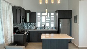 A modern kitchen with dark cabinetry, a central island, and pendant lighting.
