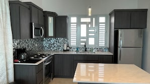 A modern kitchen with dark cabinetry, a central island, a stove, a microwave, and a refrigerator.