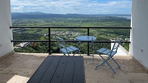 A balcony with a table and chairs, offering a scenic view of a town and mountains.