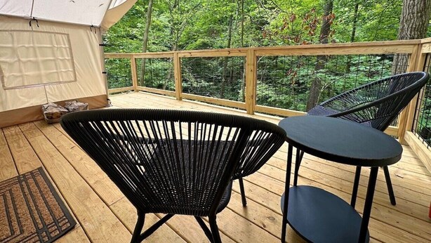 Ein überdachter Außenbereich mit Holzterrasse, zwei schwarzen Korbstühlen und einem kleinen runden Tisch.