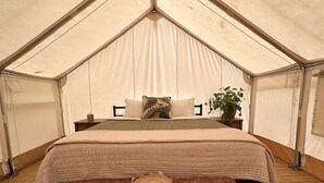 Ein Zelt-Unterkunftsraum mit einem Bett, Nachttischen, einer Bank und einem gewebten Tablett.