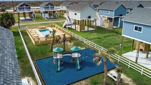 A coastal residential area with elevated houses, a playground, and a swimming pool. - Rare Community Pool! Walk to Beach! Pet Friendly (Bolivar Peninsula)
