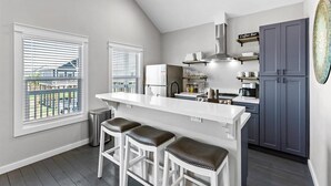 A modern kitchen with a white island, bar stools, a coffee bar, and a view of the outside. - Rare Community Pool! Walk to Beach! Pet Friendly (Bolivar Peninsula)