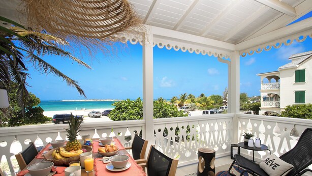 A balcony with a table set for breakfast, overlooking a beach and ocean.
