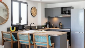 A modern kitchen with a central island, bar stools, a microwave, a coffee maker, and a refrigerator.