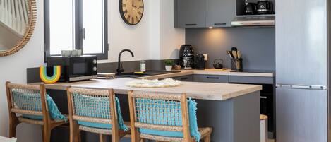 Una cocina moderna con una isla central, taburetes de bar, microondas, cafetera y refrigerador.