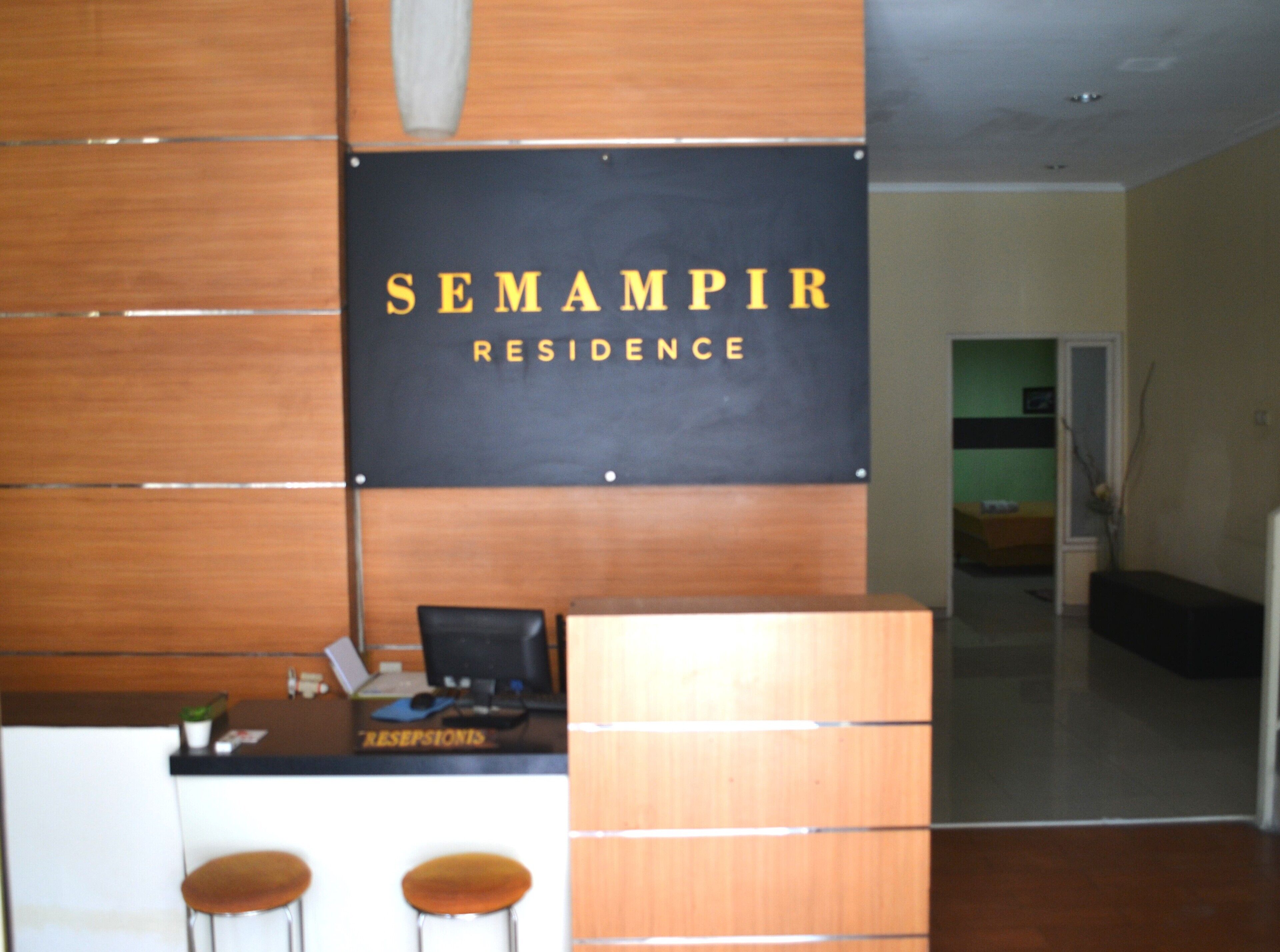 Una recepción con un cartel que dice "SEMAPIR RESIDENCE". Hay dos taburetes y una computadora sobre el mostrador.