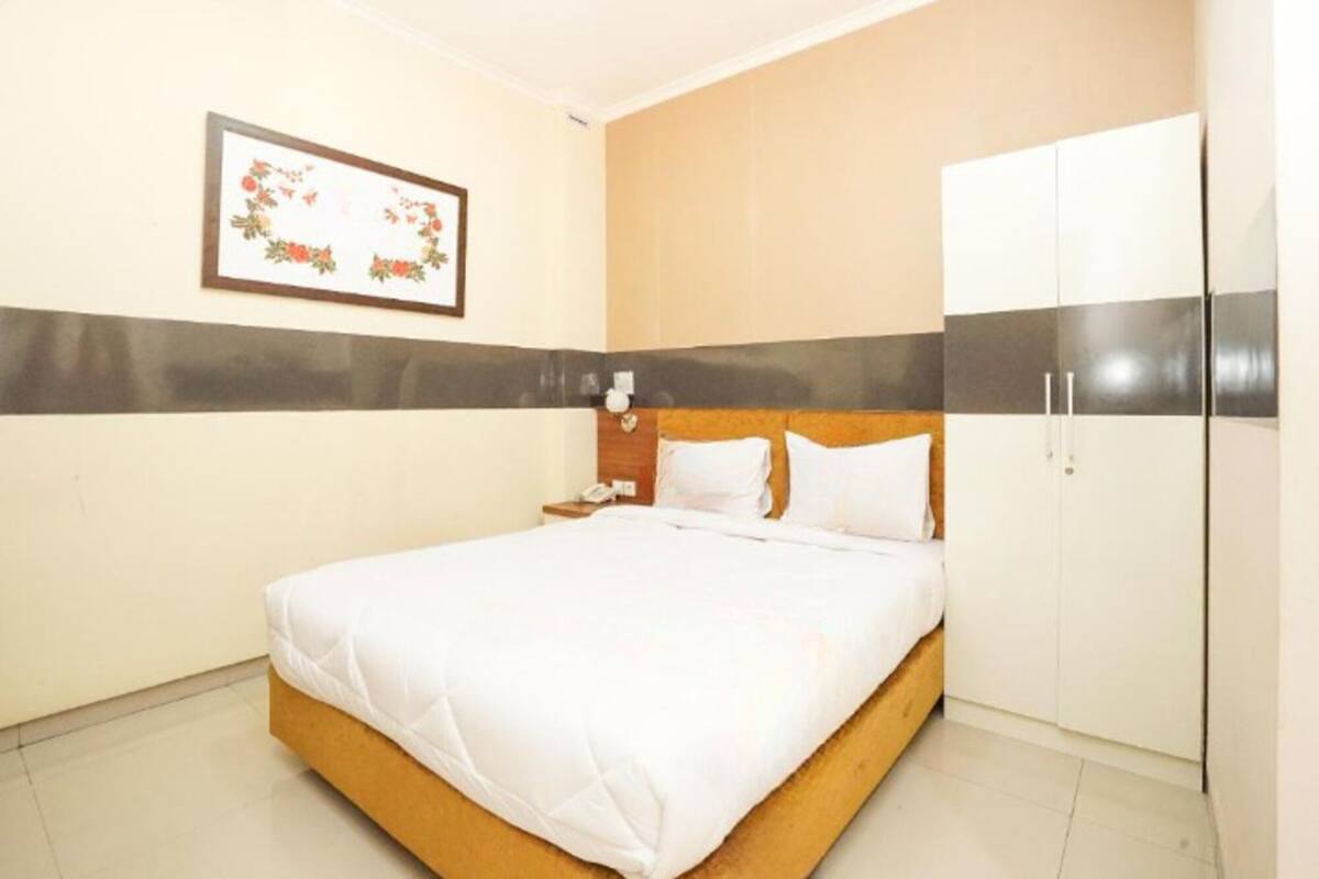 A hotel room with a bed, a nightstand, a framed floral artwork on the wall, and a wardrobe.