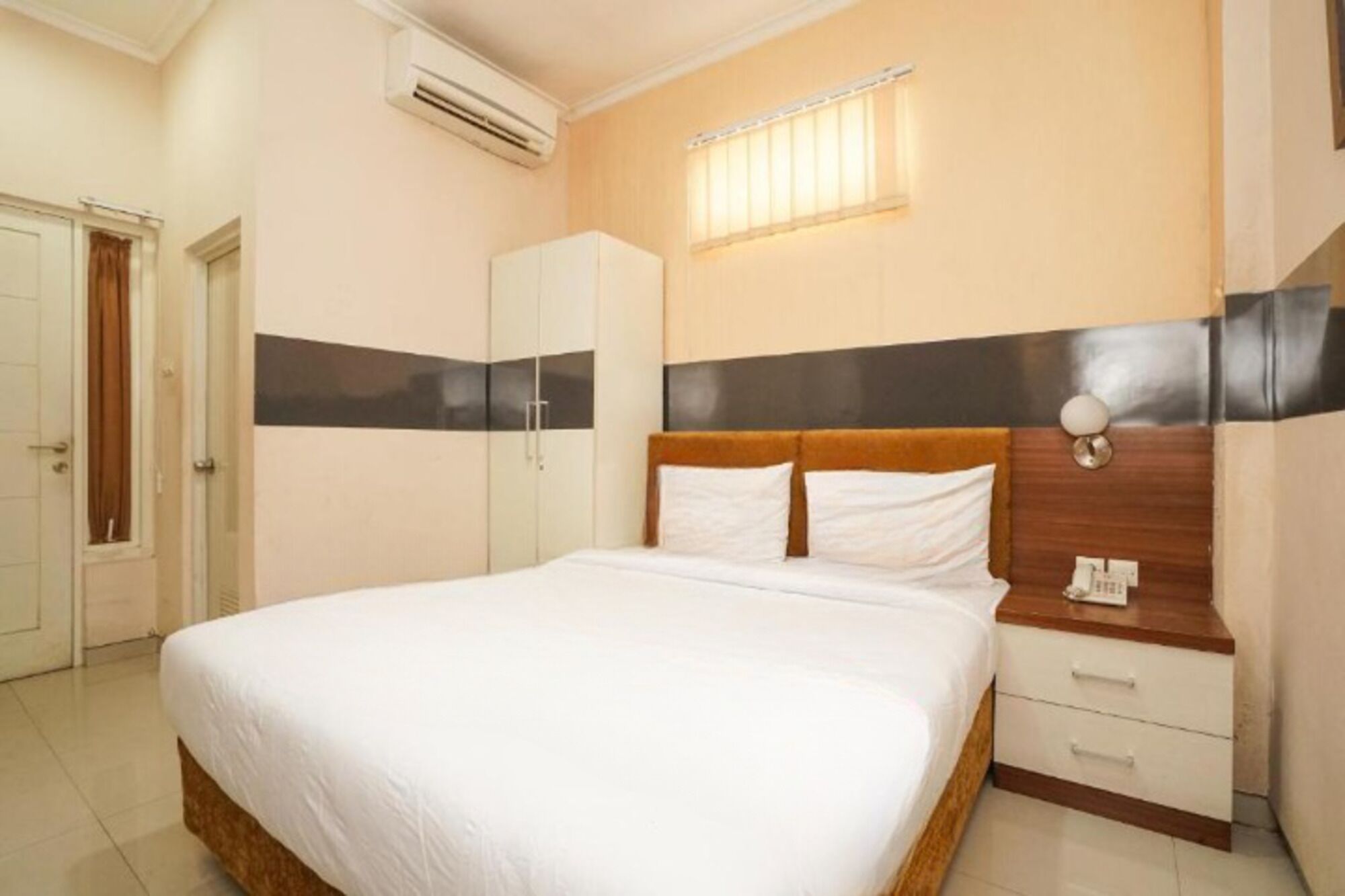Una habitación de hotel con una cama, una mesita de noche de madera, un armario y un equipo de aire acondicionado.
